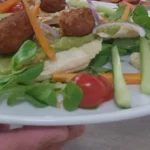 Assiette de keftas végétales sur lit de mâche, carottes, concombre et tomates cerises, tenue devant le passe