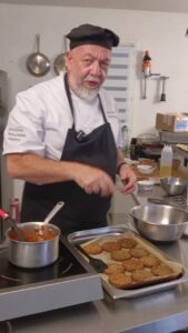 Chef à la sauteuse devant une plaque de palets végétaux, en cuisine de collectivité
