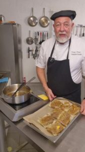 Plaque de briks dorées sur papier cuisson tenue par le chef devant une sauteuse vide