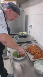Bol de keftas végétales, haricots verts et sauce au skyr en cours de dressage en cuisine de collectivité.