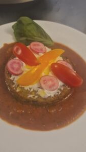 Palet végétal en entrée tiède, fromage blanc tartiné, radis taillés fin, tomates cerises et basilic sur un coulis de tomate, en gros plan.