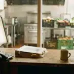 Bureau de chef de cuisine collective avec un écran, un classeur de catalogues fermé et un téléphone, la cuisine en arrière-plan