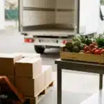 Quai de réception d'une cuisine collective avec quelques cartons, une cagette de légumes et un camion de livraison en arrière-plan